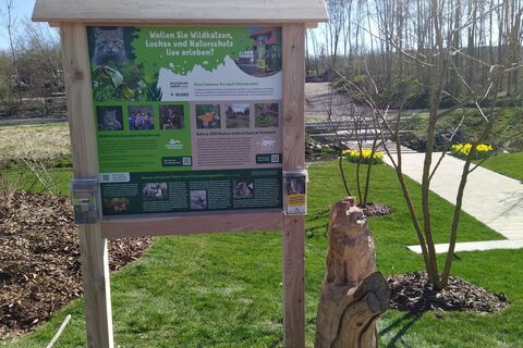 Informationstafel mit einer Holz-Wildkatzenskulptur am Rand des Hauptweges auf der Landesgartenschau Leinefelde-Worbis informiert über die Wildtierland Hainich gGmbH