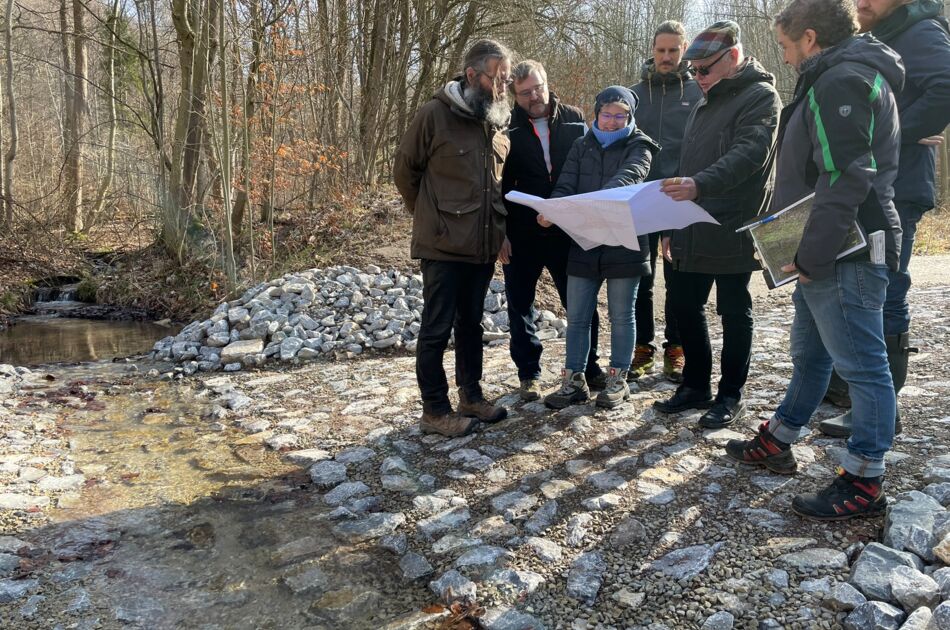 Sieben Menschen schauen an einer Furt auf einen Bauplan aus Papier